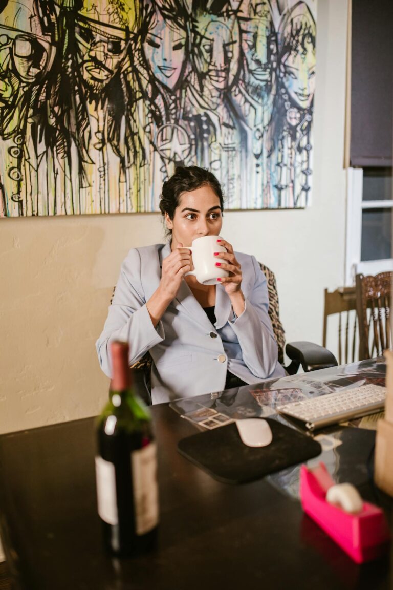Businesswoman enjoying coffee at her home office desk amidst remote work setup.