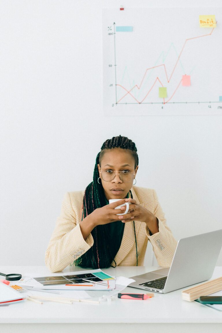 Focused businesswoman holding cup, analyzing financial data at desk.