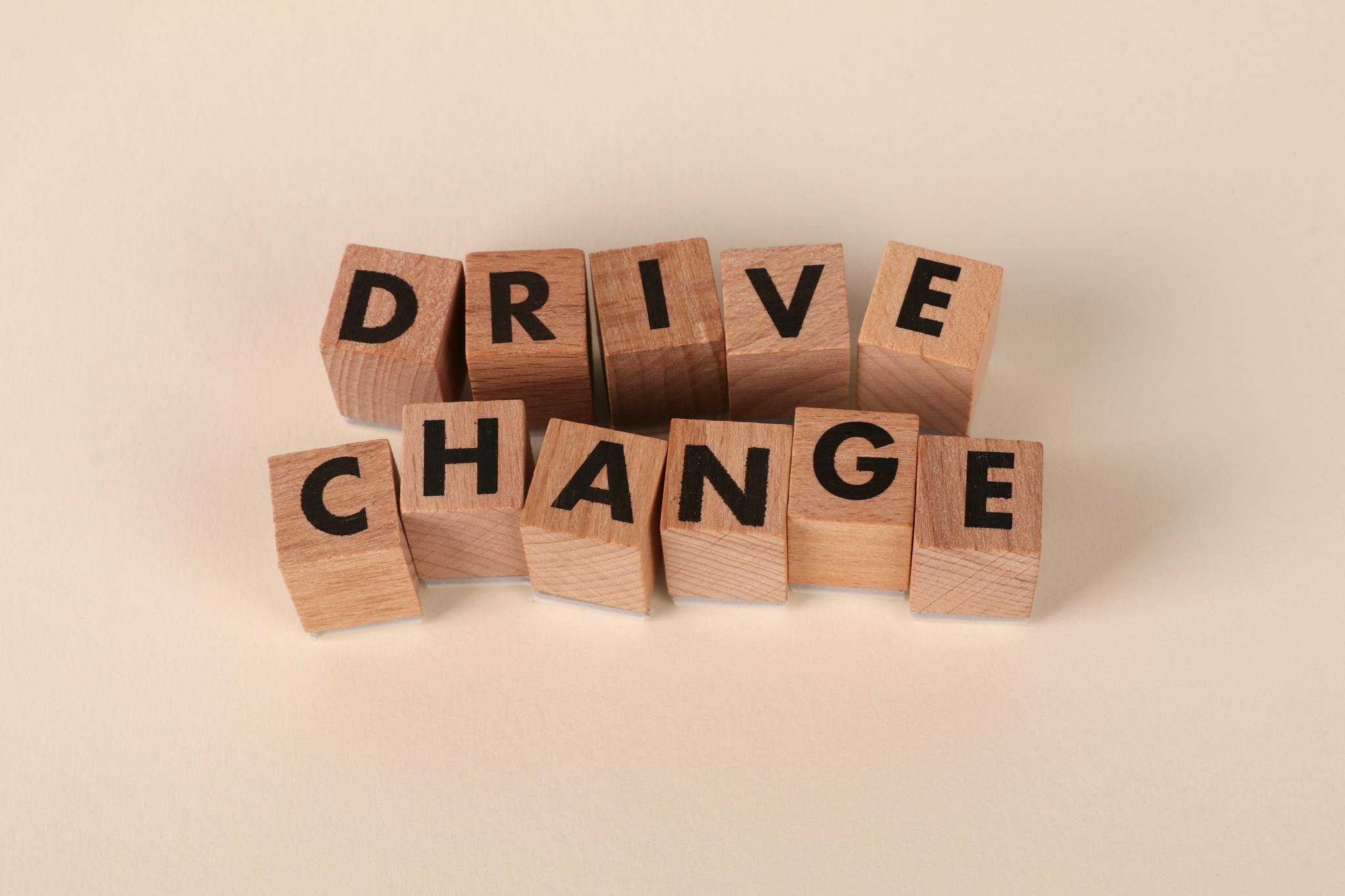 Wooden blocks spelling 'Drive Change' on a neutral background, symbolizing motivation and growth.